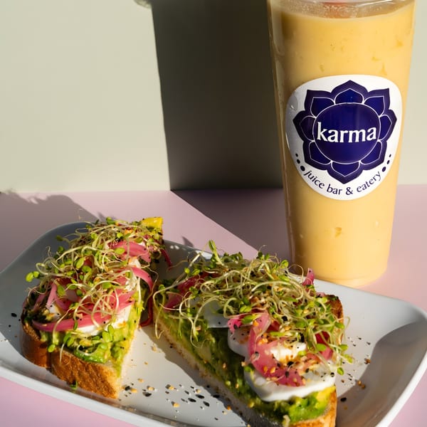 Avocado toast with sprouts and pickled onions on a white plate next to a Karma smoothie.
