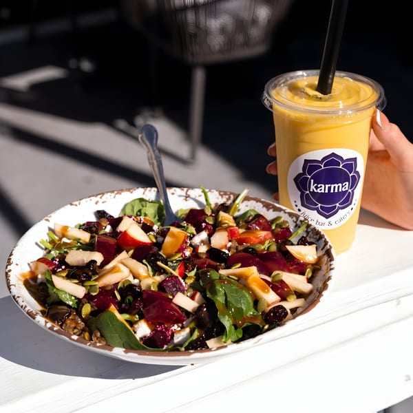 A vibrant Karma Juice Bar & Eatery salad with fruit, nuts, and dressing, next to a yellow smoothie.