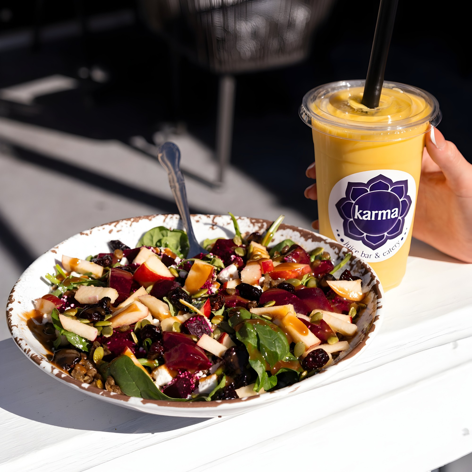 A vibrant Karma Juice Bar & Eatery salad with fruit, nuts, and dressing, next to a yellow smoothie.