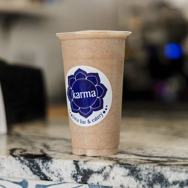 A Karma Juice Bar & Eatery smoothie in a clear cup with a blue logo on a marble counter.