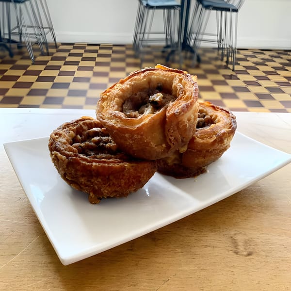 Three golden-brown pastries with nut filling on a white rectangular plate, on a wooden table.