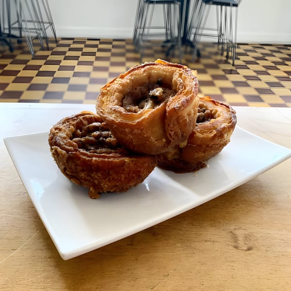 Three golden-brown pastries with nuts and powdered sugar on a white plate at Karma Juice Bar & Eatery.