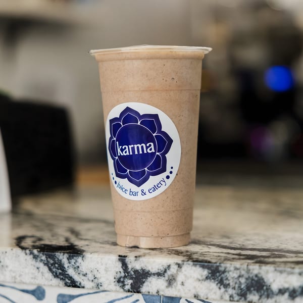A Karma Juice Bar & Eatery smoothie in a clear cup with a blue logo on a marble counter.