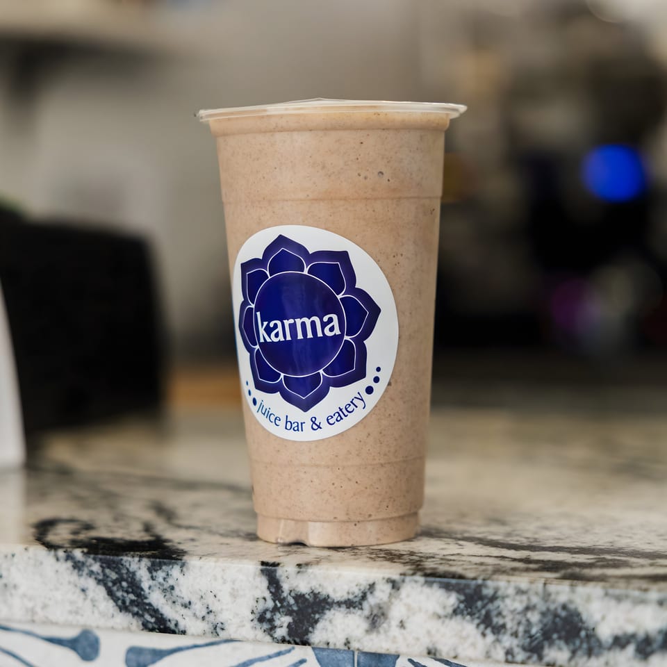 A Karma Juice Bar & Eatery smoothie in a clear cup with a blue logo on a marble counter.