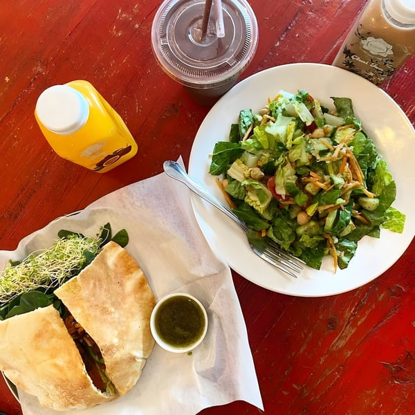 Karma Juice Bar & Eatery meal with a pita sandwich, green salad, and three drinks on a red table.
